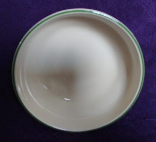 A white bowl with green trim on purple table.