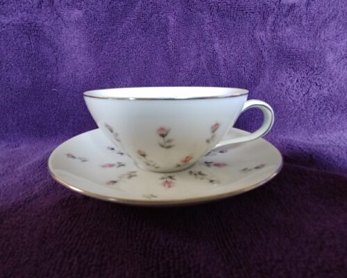 A white cup and saucer with purple flowers on it.