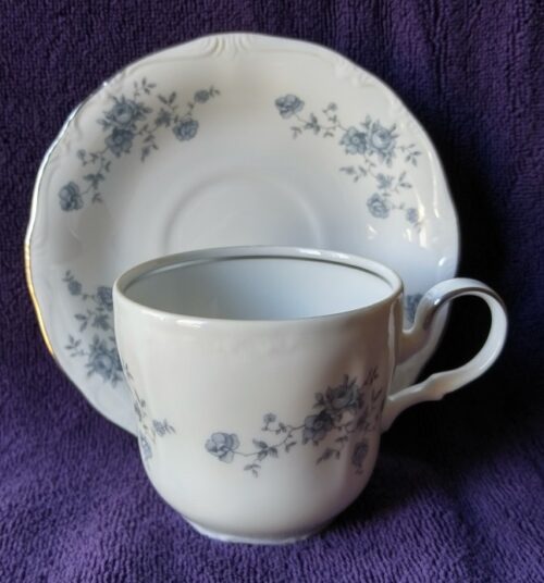 A white cup and saucer with blue flowers on it.