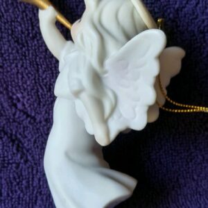 A white angel ornament sitting on top of purple blanket.