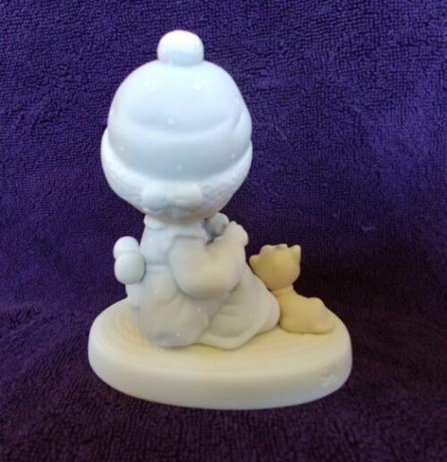 A white figurine of a baby wearing a hat and holding a teddy bear.