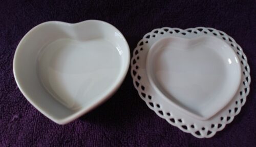 Two white heart shaped dishes sitting on a purple cloth.