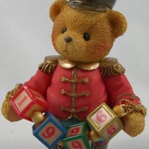 A teddy bear wearing a red uniform and holding blocks.