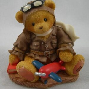 A teddy bear wearing goggles and jacket sitting on the ground.