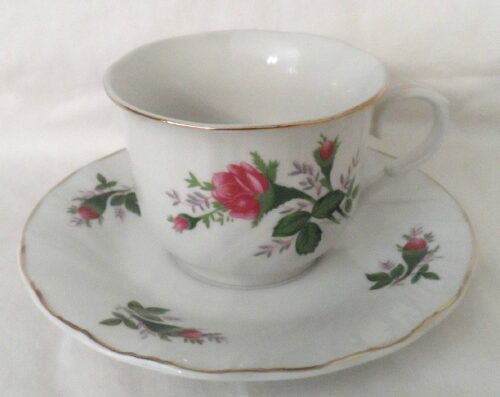 A white cup and saucer with red flowers on it.