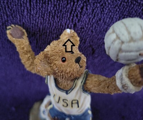 A teddy bear is holding a ball in his hand.