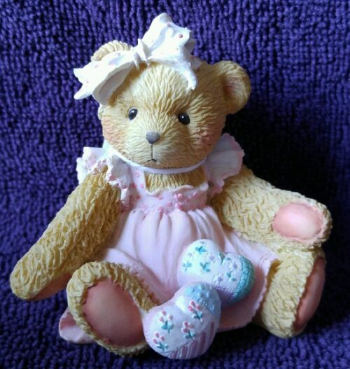 A teddy bear with pink dress and bow on it's head.