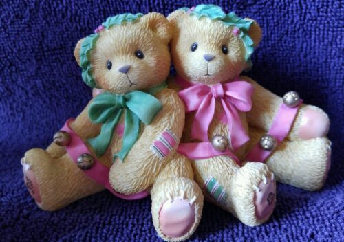 Two teddy bears sitting on a purple blanket.