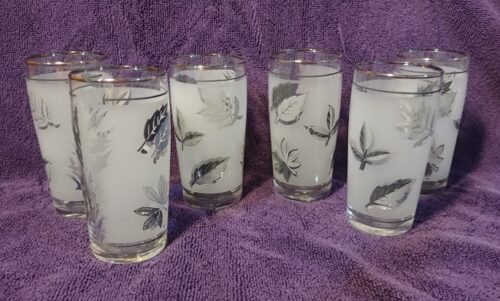 Four glasses with leaves on them are sitting on a purple cloth.