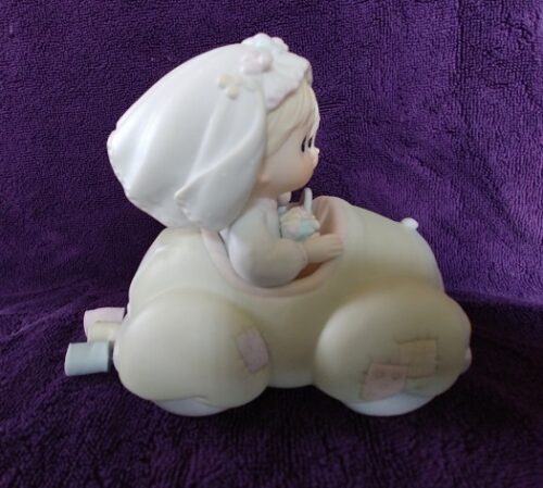 A white ceramic figurine of a baby in a car.
