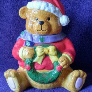 A teddy bear wearing a santa hat and holding a wreath.