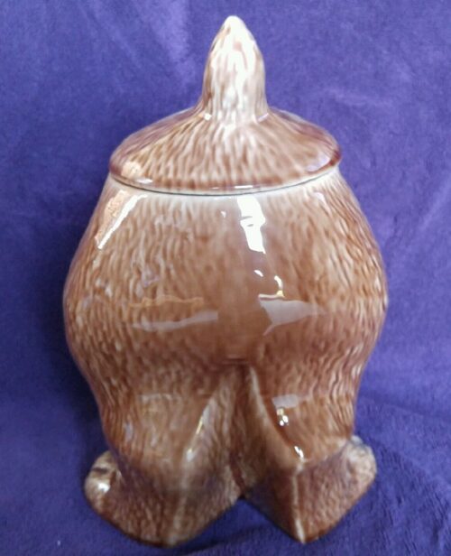 A brown ceramic bear with its back legs crossed.